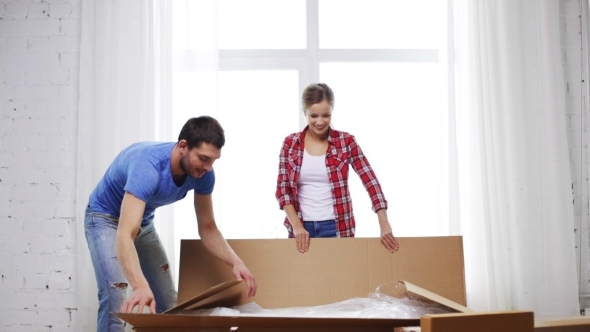 Smiling Couple Opening Big Cardboard Box At Home