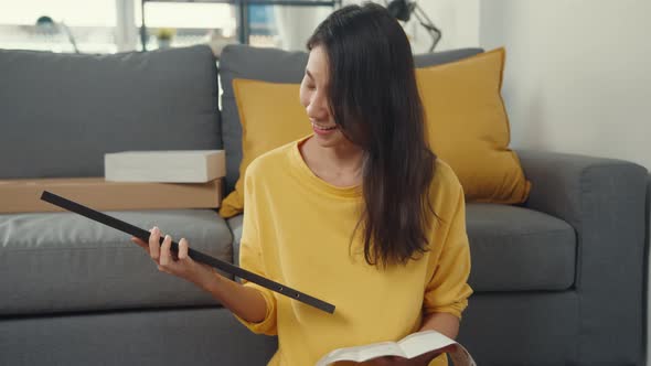 Happy asian young woman unpacking box and reading the instructions to assemble new furniture.