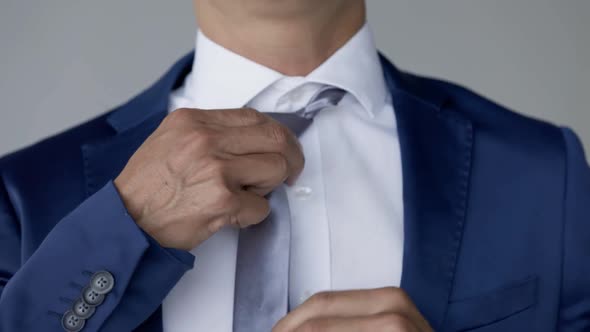 Caucasian male puts tie in place on white collared shirt, formal wear