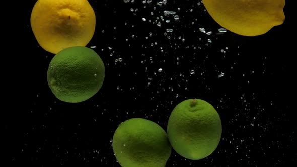 Slow Motion Lemon and Lime Falling Into Transparent Water on Black Background