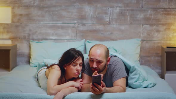 Husband and Wife Using Phone While Laying in Bed