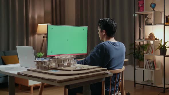 Asian Male Engineer With The House Model Working On A Mock-Up Green Screen Desktop At Home