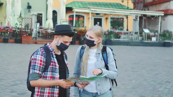 Young Tourists Couple in Protective Masks Using Map on Central City Square