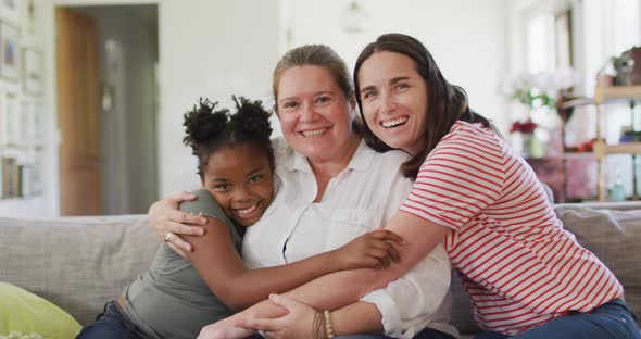 Portrait of happy caucasian lesbian couple and their african american daughter embracing and smiling