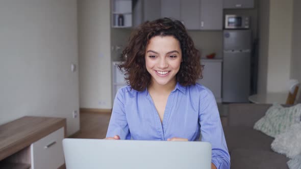 Happy Latin Young Woman with Curly Hair Talking with Friends on Laptop Computer