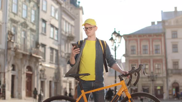 Portrait of a Happy Delivery Man Who is Standing and Texting on a Smartphone