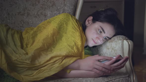 A Girl Uses the Mobile Phone Apps in the Evening Lying on the Couch