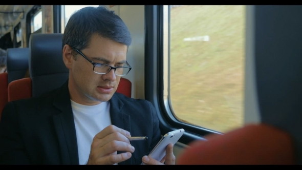 Young Man Using Cell To Browse Online In Train