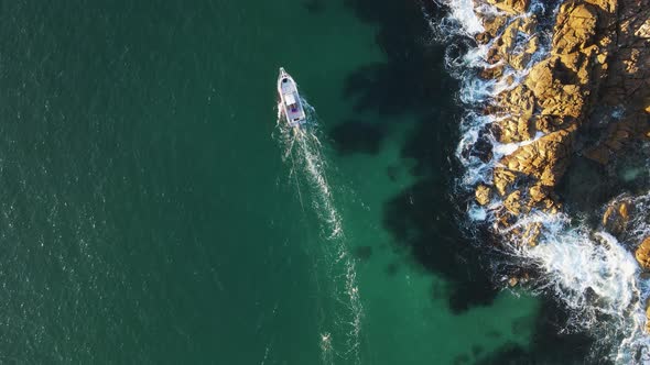 A fishing boat trawling for schools of mullet around a rugged coastal headland. High drone view look