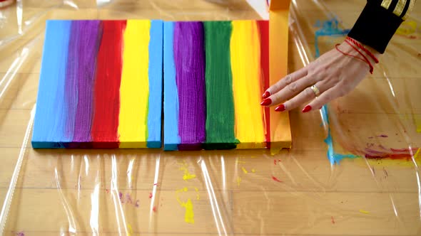 A woman using painters tape to finish her colorful stripes on a canvas