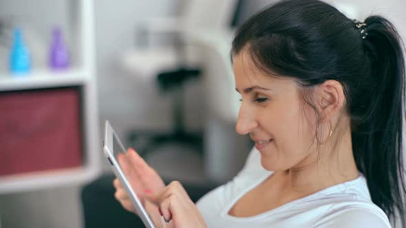 Beautiful Woman Using Tablet Sitting on Sofa at Home