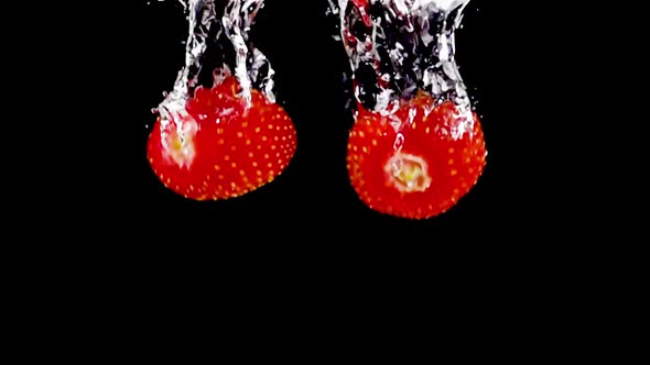 Super slow motion, fresh ripe strawberries fall into the water with air bubbles