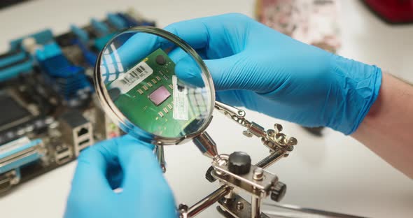 Closeup of Assembling Motherboard Fixing Details with Magnifying Glass and Tweezers in Protective