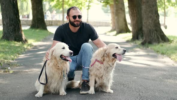 Blind Man with Guide Dogs Sitting on Sidewalk in Park