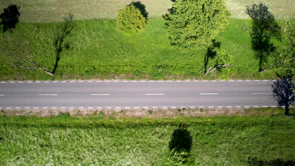 Aerial drone flying over lush green fields next to the road.