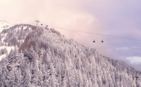 Aerial view over snowy mountain ridge valley with clouds, cable car lifting. Ski Gondola Lift