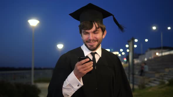 Graduate Student Walking in the Evening and Texting Message on the Phone