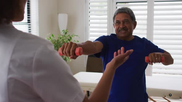 Mixed race female physiotherapist helping senior man exercise using dumbbells