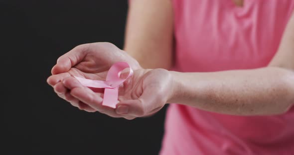 Mid section of woman holding a pink ribbon against black background