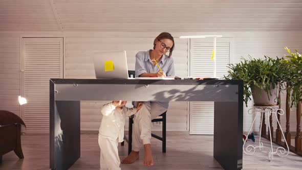 A Young Mother is Working at Home Using Computer While She's Taking Care of Her Baby