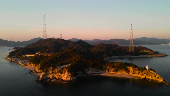 Backwards Aerial Drone movement over island with lighthouse and powerlines at sunset