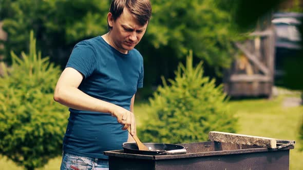 Close-up, Slow Motion: Man Cooks Pilaf, in a Cauldron, on Coals, on a Grill. Stir the Meat