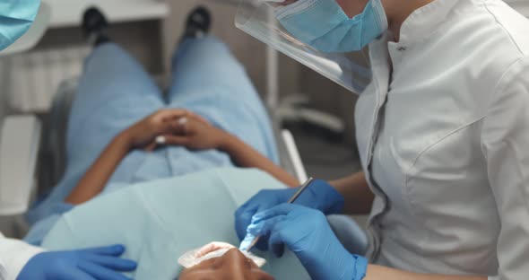 Man Dentist Supervising Female Assistant Operating African Woman in Dental Clinic