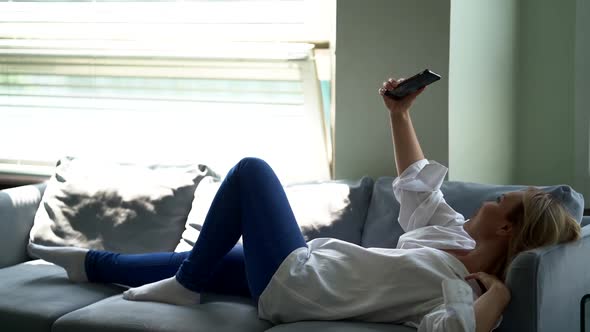 Blonde Woman Is Taking Selfie By Smartphone, Lying on Couch at Home, Day at Weekend