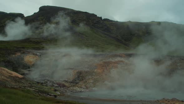 iceland landscape, geothermal hotspring steam smoke rising, distant figure of photographer taking a