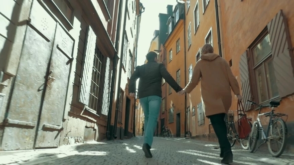 Happy Couple Running Along The Narrow Street