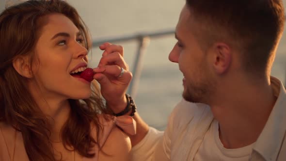 Handsome Guy Feeding Beautiful Attractive Longhaired Girl with Strawberry While Sailing on Yacht at