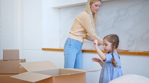 Funny little girl with long plaits unpacks brown cardboard box and gives mother white plates