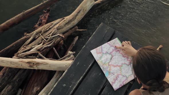 Woman Is Choosing Place To Visit on Map Resting on Sea Pier at Sunset