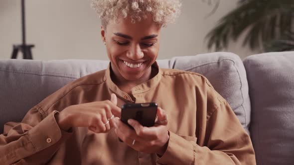 Smiling African Female Relaxing on Cozy Sofa Using Smartphone Received Message