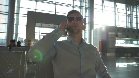 Young Smiling Businessman Talking on Phone at Airport with Sun Flare at Background. Close Up