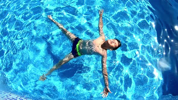 Young boy in the swimming pool. Teenager lying on his back on the water surface in a sunny day. 