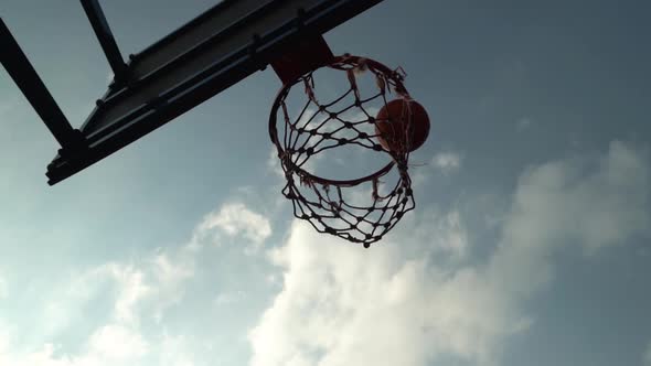 Orange Basketball Bounces Off Backboard and Scores Hitting the Basket on an Outdoor Court in the