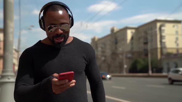 Portrait of an African Man in Dark Clothing, Sunglasses and Headphones. He Holds a Red Phone in His