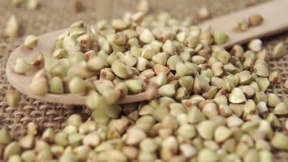 Grains of green buckwheat fall in slow motion onto a wooden spoon