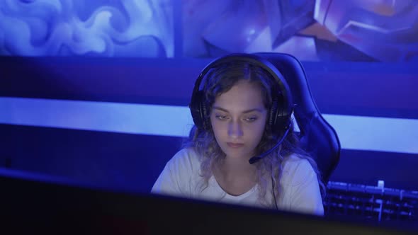 Young Woman Sits in Headphones at a Modern Computer Club, Plays an Online Game. Woman Smiles and Is