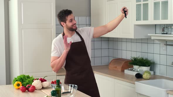 Man in an Apron Takes a Selfie While Standing in the Kitchen Before Preparing a Vegan Meal