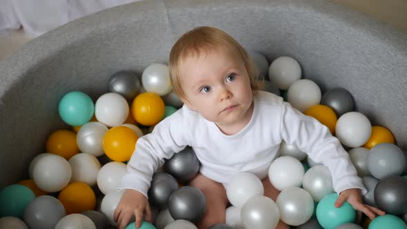 Girl in a White Bodysuit Plays with Colorful Plastic Balls in Dry Pool