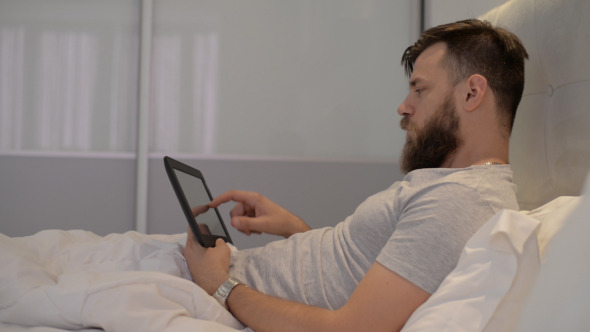 Man Using Tablet in Bed
