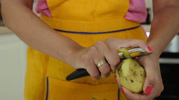 A Woman With Orange Manicure Peeling a Potatoes