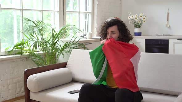 A Male Italian Football Fan Watches TV at Home with the Flag of Italy