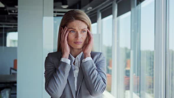 Corporate Businesswoman in Formal Suit Standing in Office Having a Bad Headache