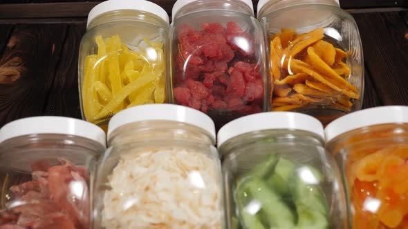 Glass Jars with Various Dried Fruits on a Brown Wooden Background