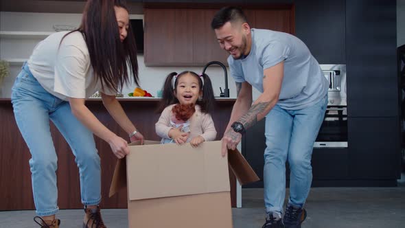 Cheerful Asian Parents Riding Baby Girl in Cardboard Box