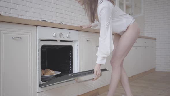 Young Caucasian Woman Opening Oven and Taking Out Plate with Delicious Croissants. Happy Brunette