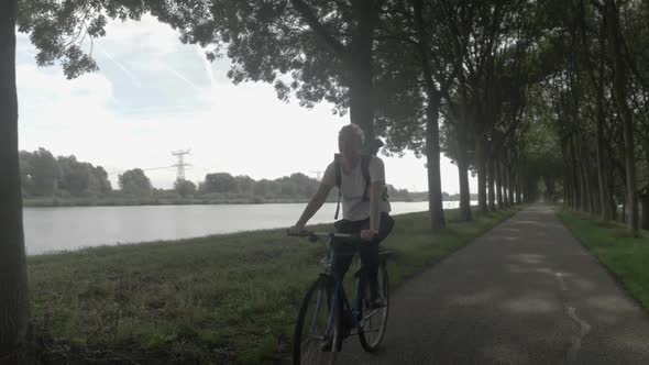 Pretty young blonde girl with backpack riding a bike on bike path in Myrte-boerderijen. Netherlands.